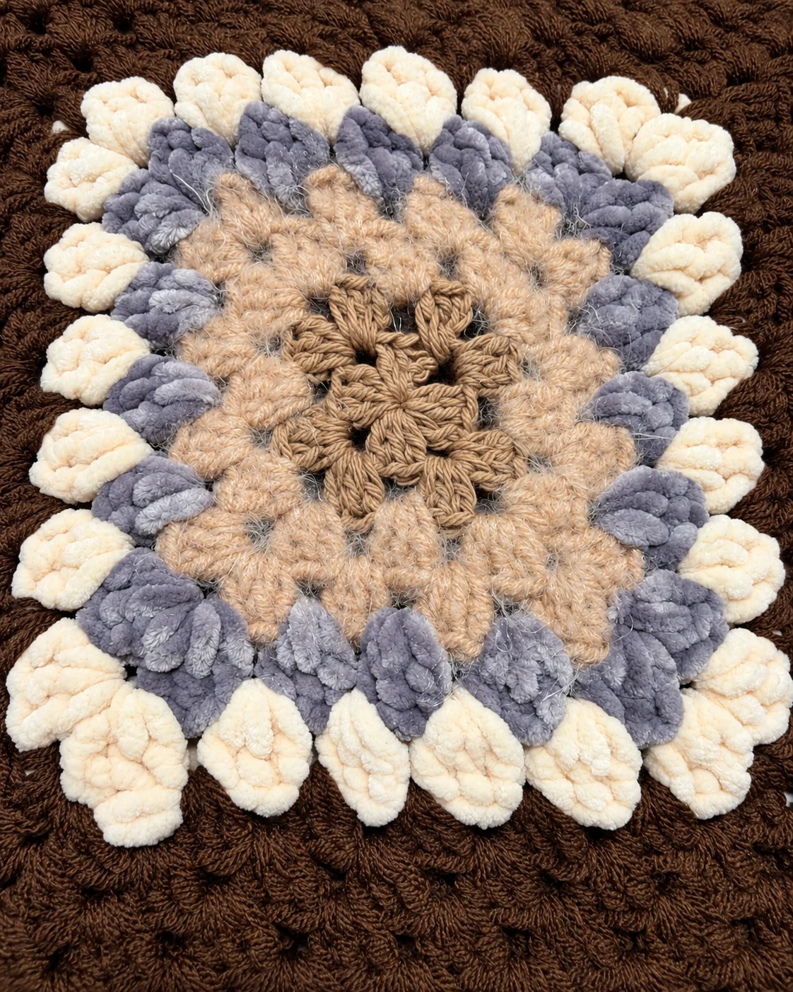 Close-up of a raised crochet flower in cream, muted lavender and warm beige on the cocoa brown cardigan