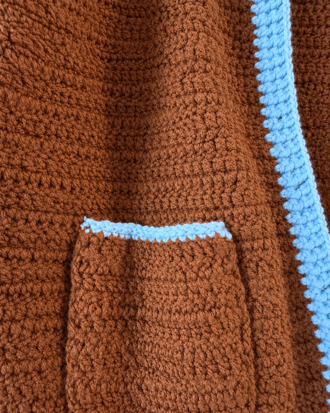 Close-up of the chestnut-brown crochet pocket with sky-blue trim